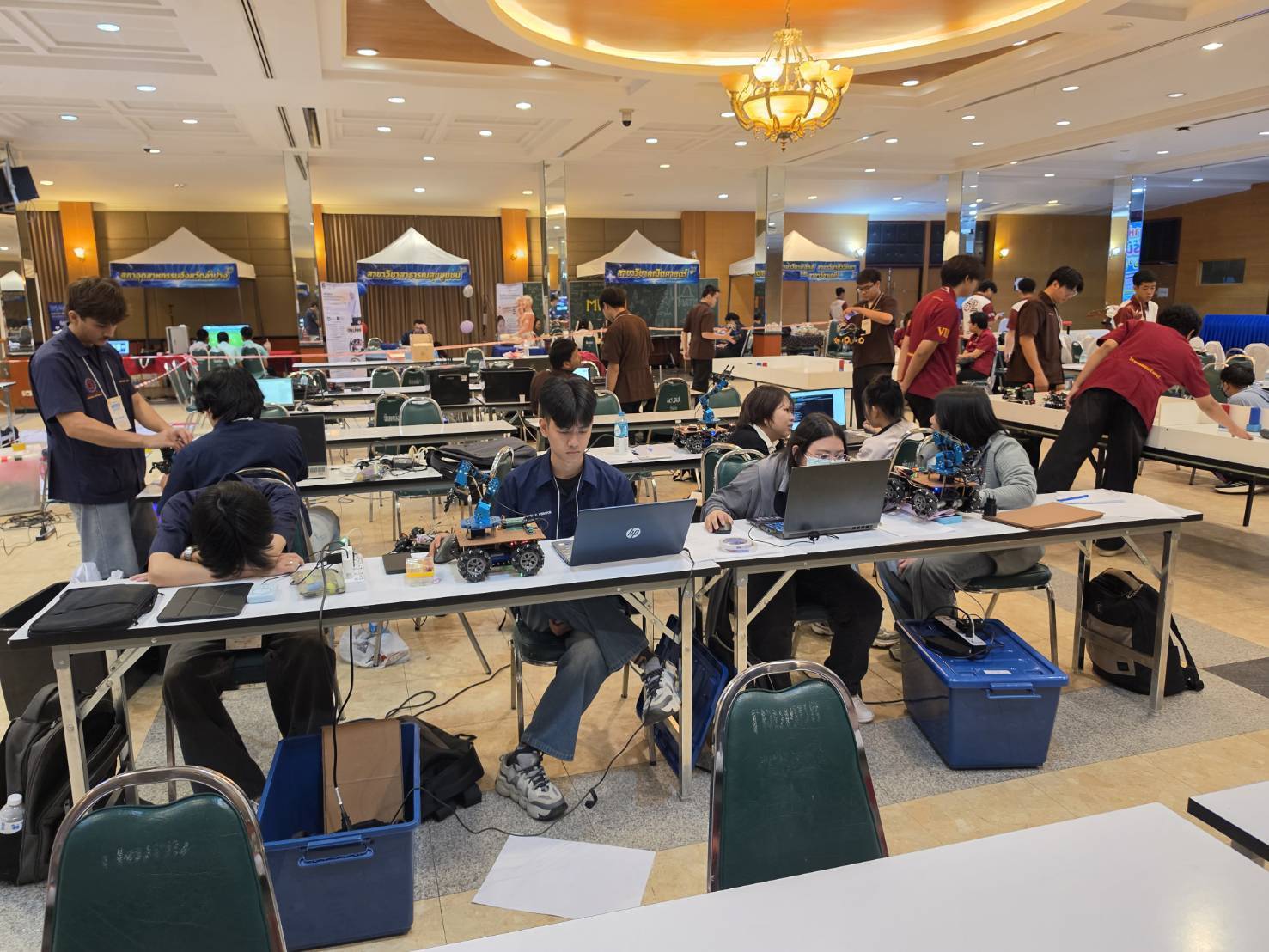 Student teams working at laptops on their competition robots in the pit area at Lampang Rajabhat University