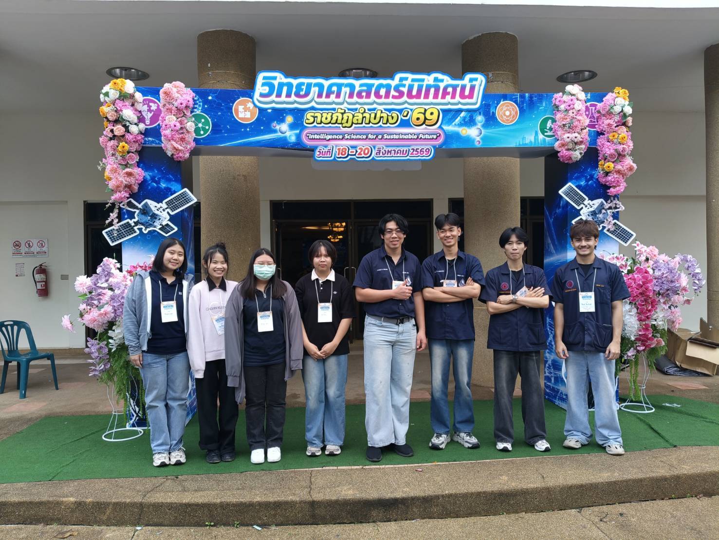 Eight ISL students standing beneath the Lampang Rajabhat science exhibition banner, 18-20 August 2026