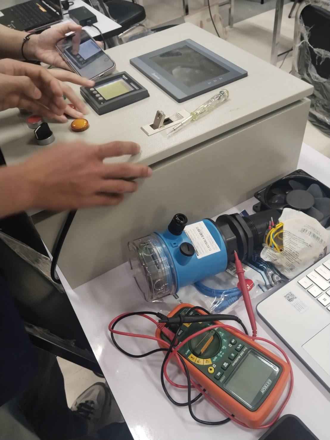 Workbench with an electromagnetic flow sensor, handheld HMI terminal and a digital multimeter used in the bootcamp labs