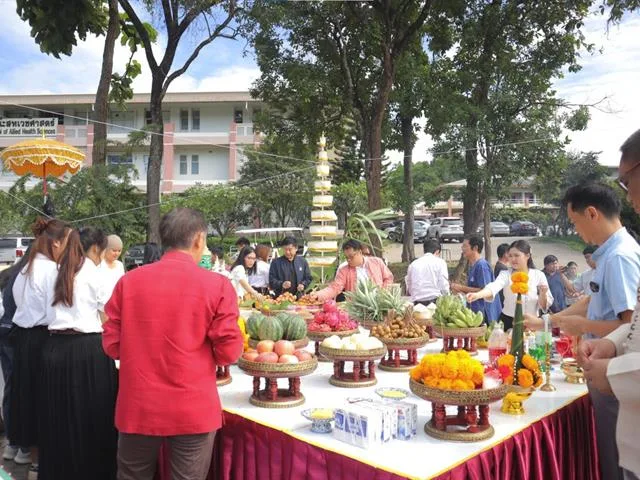 Alumni, students and staff gathered around an offering table laid with fruit and marigold garlands