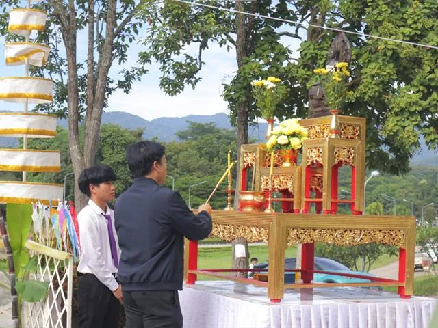 Two participants making an offering at the shrine canopy, with the Phayao hills behind them